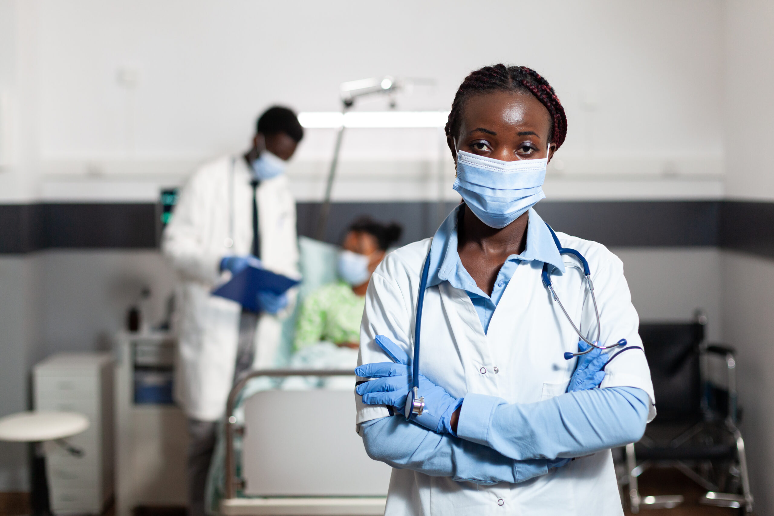 Portrait of african american woman working as doctor in hospital ward clinic. Afro doctor wearing coat, gloves, stethoscope and face mask for protection. Black medic looking at camera
